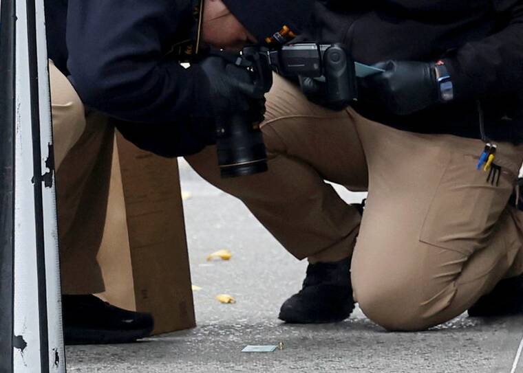 SHANNON STAPLETON / REUTERS
                                A member of the NYPD Crime Scene Unit takes a picture of a shell casing found at the scene where the CEO of UnitedHealthcare Brian Thompson was reportedly shot and killed in midtown Manhattan today.