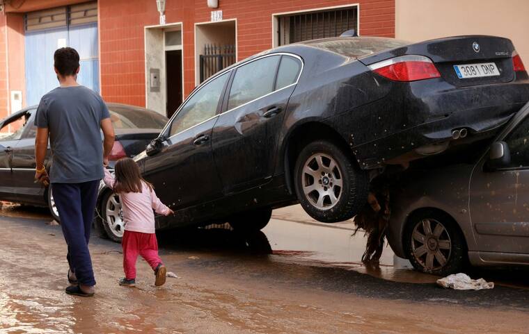 REUTERS/EVA MANEZ
                                People walk on a street next to damaged cars after torrential rains caused flooding in Guadassuar, Valencia region, Spain, today.