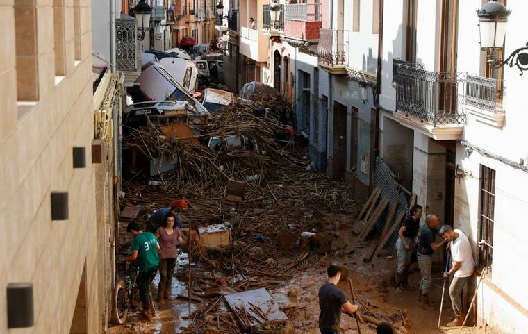 REUTERS/EVA MANEZ
                                People work to clear a mud-covered street with piled-up cars after torrential rains caused flooding in Paiporta, Spain, today.