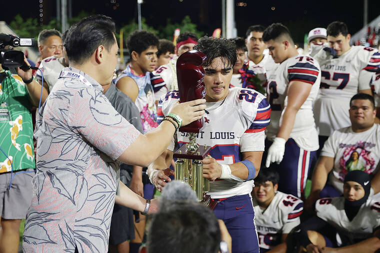 ANDREW LEE/ SPECIAL TO THE STAR-ADVERTISER
                                Saint Louis’ Charles-Titan Lacaden (22) receives the championship trophy after winning the HHSAA Open Division Football Championship Game 17-10 over Kahuku on Friday at Clarence T.C. Ching Field in Honolulu.